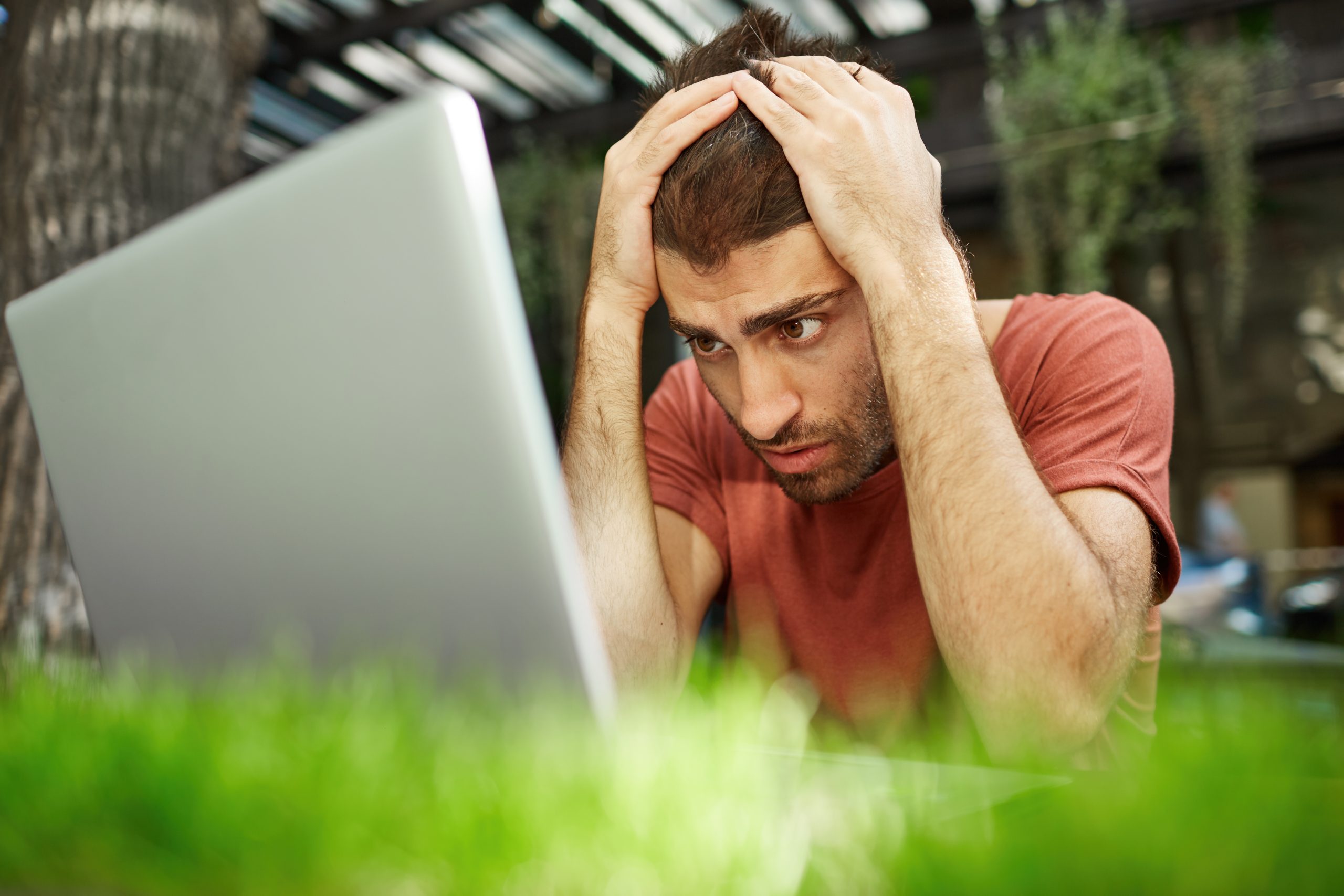 Worried young male worker with stylish hairstyle having anxious desperate look while facing deadline but failing to finish report in time. Good-looking guy desperatly squeezing his head.